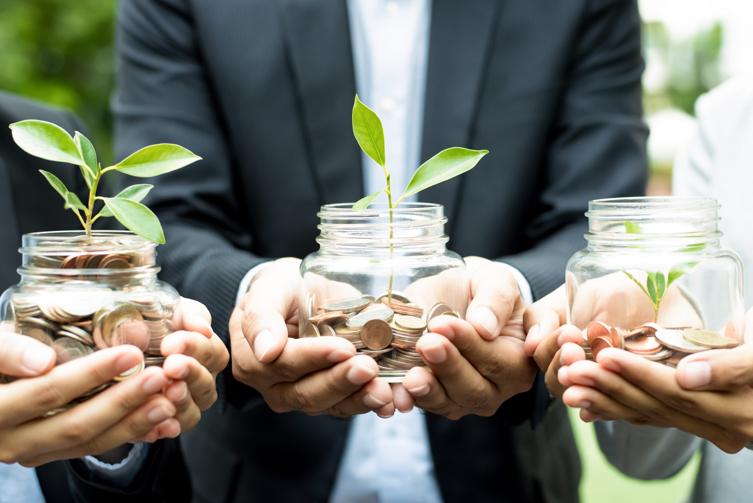 Business people holding glass jars with plants growing from money - investment and financial metaphor